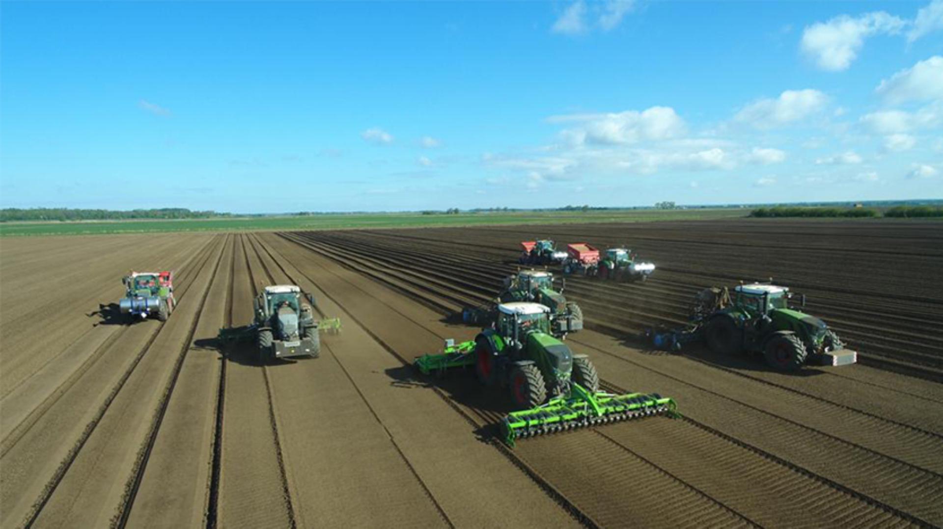 Long view of farm machinery being driven in fields 