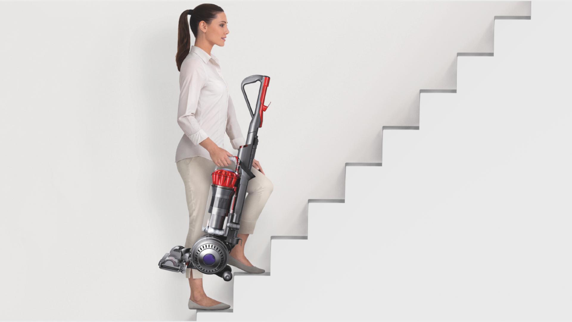 Woman carrying an upright vacuum up a set of stairs.