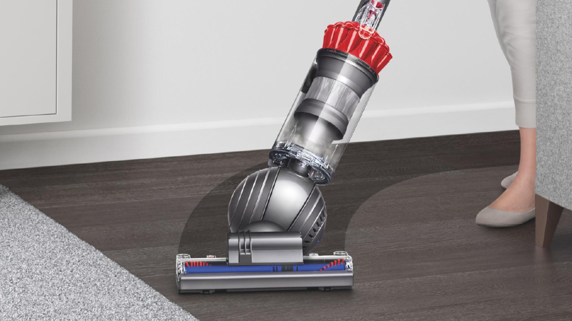 Upright vacuum cleaner being steered in a sweeping arc across a black hard floor surface. 