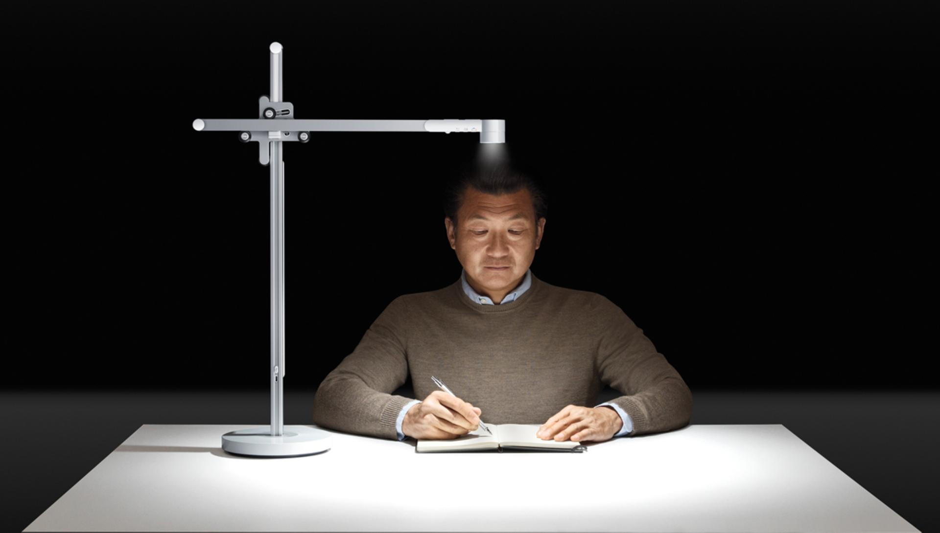 Older model using Dyson Lightcycle light at his desk to work