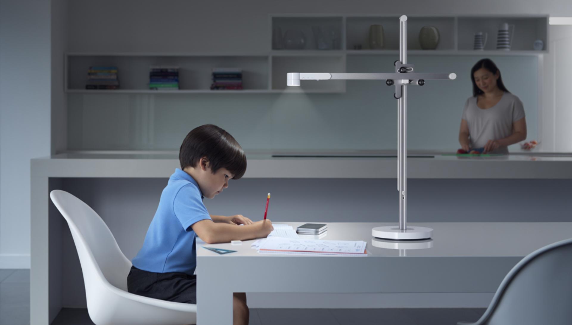 Child working at a table under light from the Dyson Lightcycle desk light