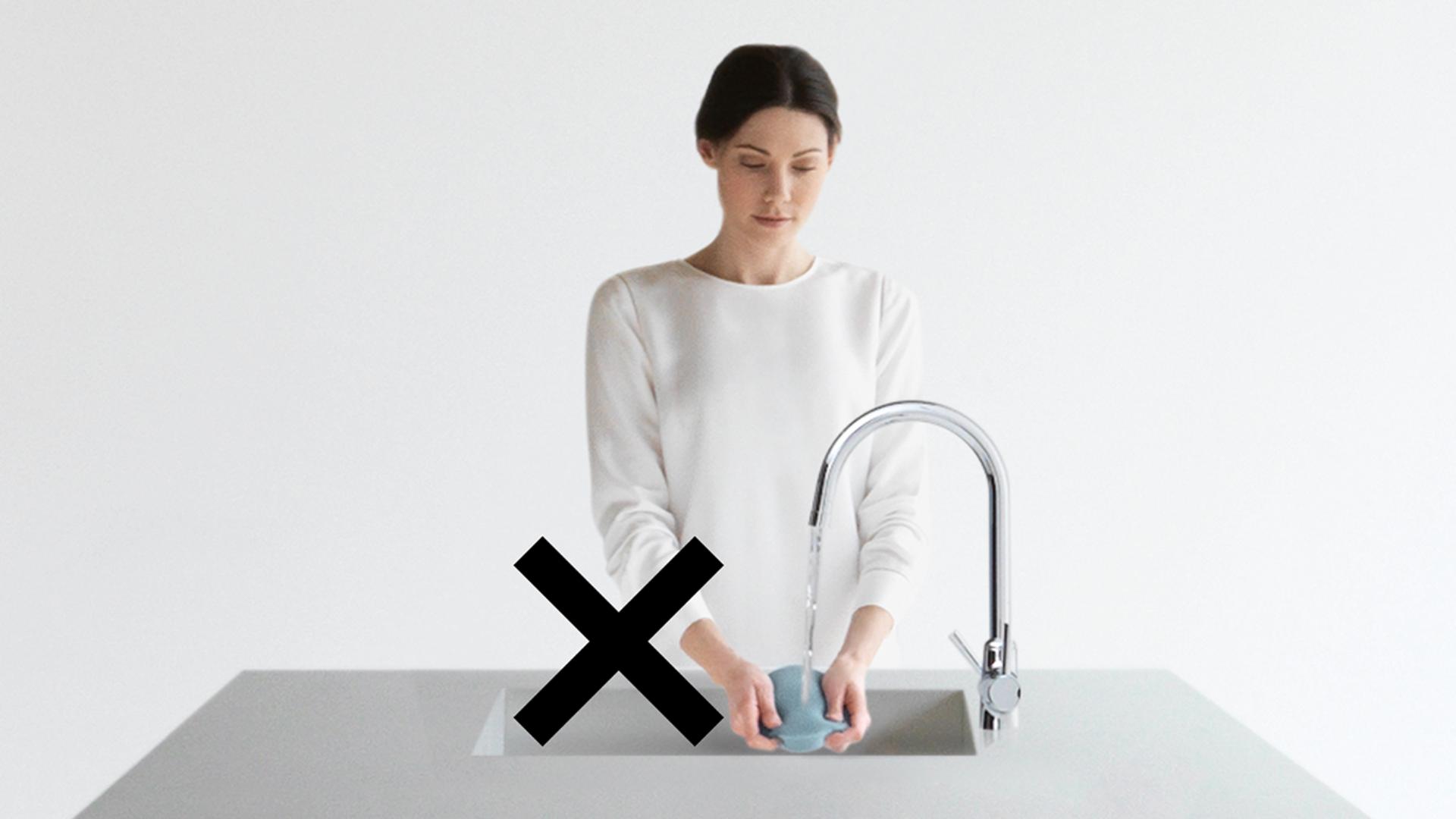 A woman washing a vacuum filter in the sink, crossed out.